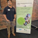 APEX 2024 Zach Landon-Lane Young engineer Zach Landon-Lane of Connectics stands beside APEX banner